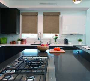 Modern kitchen with a black countertop, gas stove, and marble backsplash. A bowl of apples and a cutting board with oranges add a pop of colour. Two windows with fabric blinds are above the sink, enhancing the room's aesthetic.