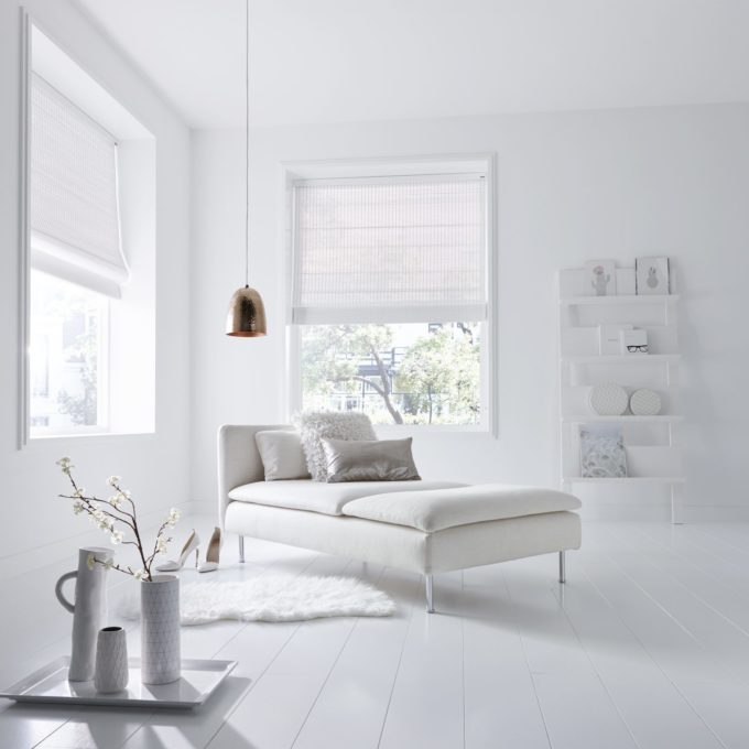 Bright, minimalist room with a white chaise lounge, pendant light, and vases. Fabric blinds adorn the large windows, harmonizing with white shelves to complete the serene setting.