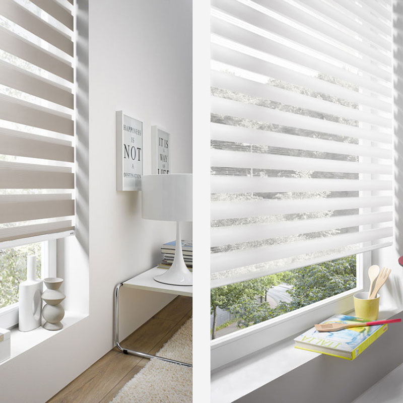 The room showcases elegant Zebra Blind Range B in white, a cozy chair, and a stylish lamp, accented by decorative items on the window sill. Motivational prints adorn the walls, while trees outside add a splash of natural color through the blinds.