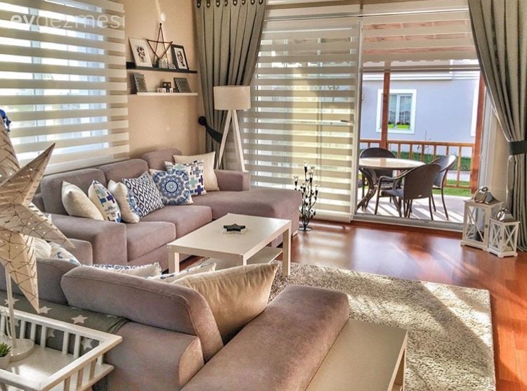 Modern living room with gray sofas, striped curtains, and colorful pillows. A sleek coffee table sits on a fabric rug, and large sliding doors feature Zebra Blind Range B, opening to a patio with outdoor seating.