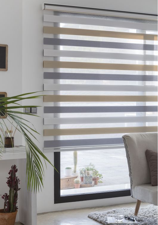 Partially open Zebra Blind Range B reveals potted plants outside the window. An indoor plant and part of a chair are visible in the foreground, adding to the tranquil scene.