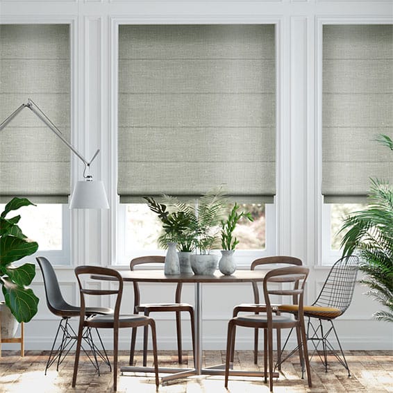 Dining area with a round table, six chairs, and gray blinds on windows. Potted plants adorn the table and floor. A modern lamp elegantly hangs above the table.