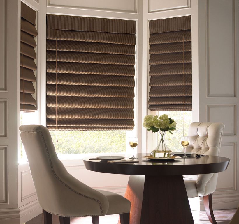 A table with two upholstered chairs, set with dining essentials and a vase, is in a room where the windows are accented by Roman Blind Range A.