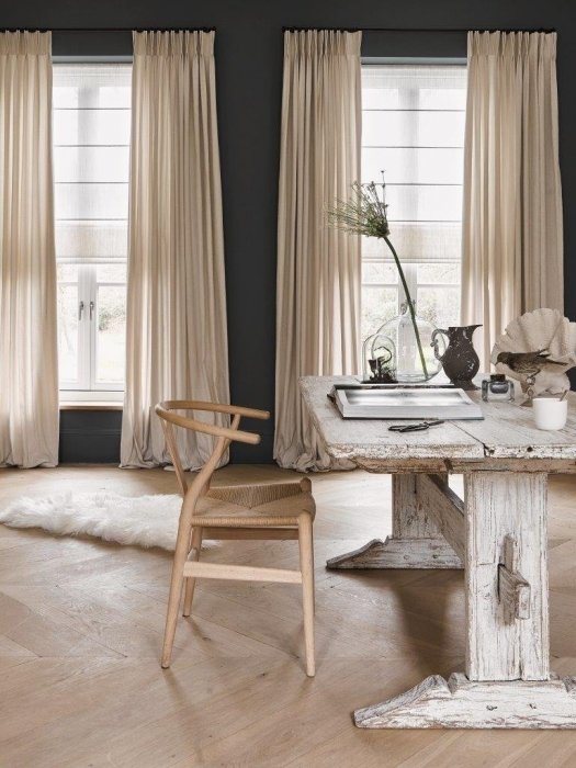 Minimalist study with a wooden table, chair, and decor items, set against elegant fabric curtains in soft colors and large windows.