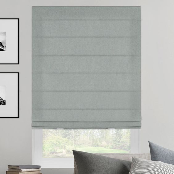 A sleek gray roman shade made from premium fabric partially covers the window, while two framed black and white photos elegantly hang on the adjacent wall.