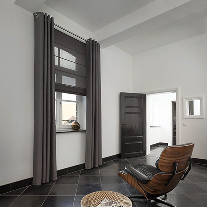 A modern room featuring a sleek black lounge chair upholstered in rich fabric, complemented by a large window dressed in dark blinds. The setting is completed with a black door and elegant tiled floor.