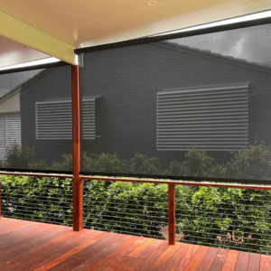 A covered patio with wooden flooring and wire railing features a partially lowered Straight Drop Blind, facing a neighboring house with louvered windows.