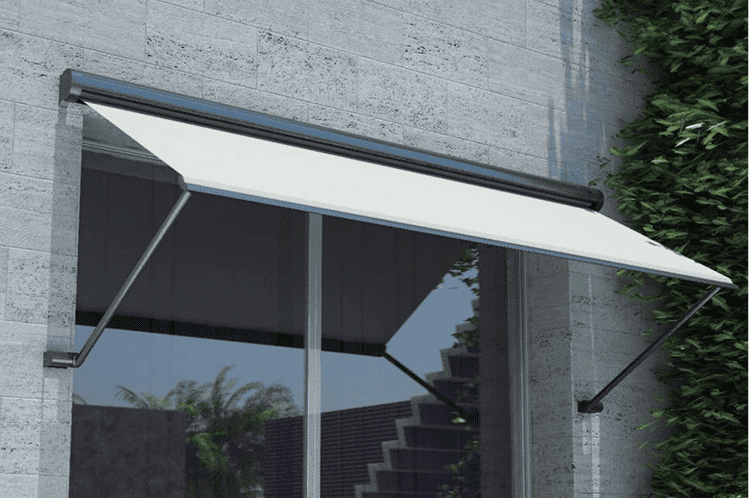 White retractable awning mounted above a large glass window on a stone building, with greenery visible on the right side.