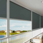 A row of closed Deep Channel Blinds covers a screened porch overlooking a lake and houses on a sunny day.
