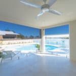 Spacious room with a ceiling fan and large windows overlooking a pool and waterfront view. Planters and modern furnishings enhance the bright, open space.