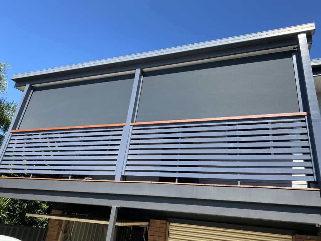 Outdoor balcony with dark privacy screens fully lowered, horizontal slat railing, and a clear blue sky in the background.