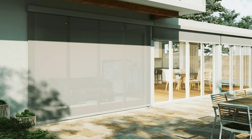 A modern patio features sliding glass doors, an outdoor table and chairs, and partially lowered Outdoor Wired Guide Blinds that shade the interior living space.