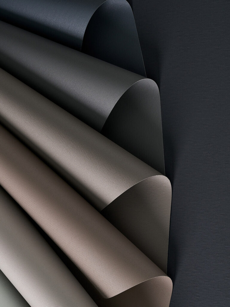Curved sheets of textured paper or fabric in varying muted shades, arranged in a fanned pattern on a dark background.