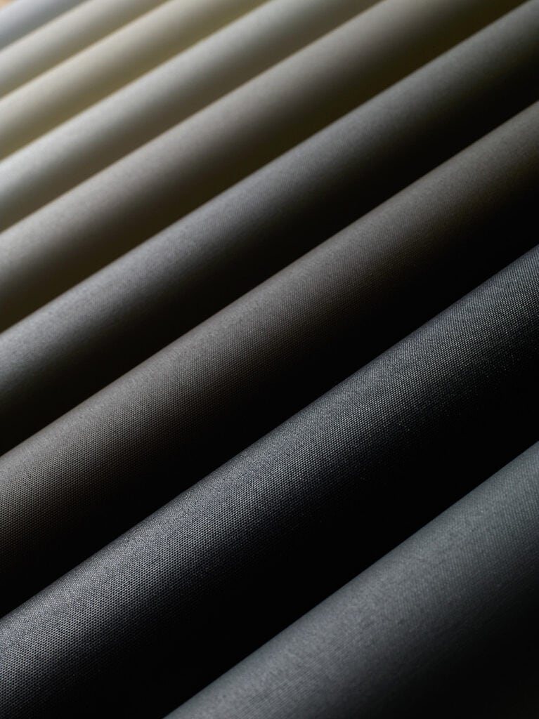 Close-up view of evenly spaced, cylindrical fabric rolls in shades of black and grey, arranged diagonally and lit from above.
