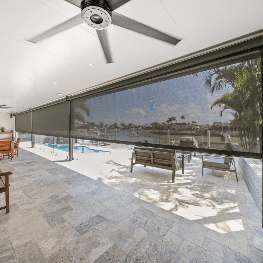 Covered patio area with ceiling fans, stone flooring, and a retractable screen overlooking a pool, outdoor seating, and waterfront view.