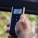 A hand holding a black remote control with a digital display showing the number 2 and several navigation buttons.