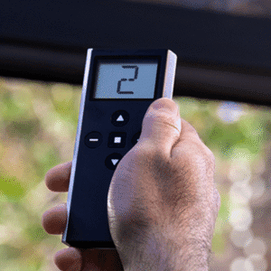 A hand holding a black remote control with a digital display showing the number 2 and several navigation buttons.