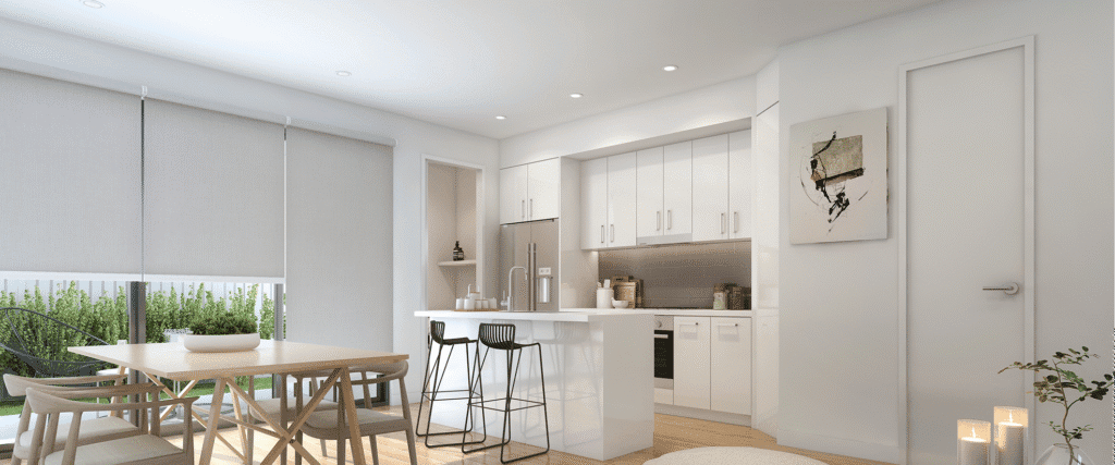 A modern kitchen with white cabinets, a small island with two black stools, a wooden dining table with chairs, large windows with blinds, and candles on the floor.