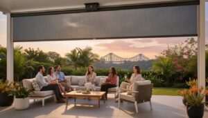 Six people sit and converse on a covered patio with a view of a bridge in the background, surrounded by greenery and potted plants at sunset.