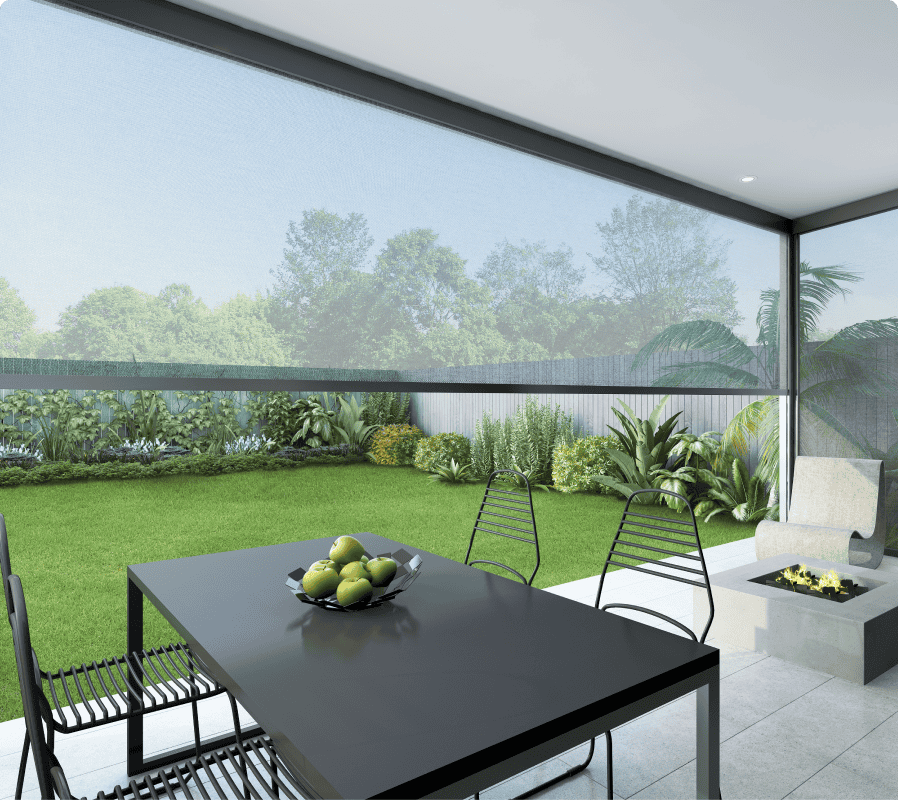 Modern patio with a black dining table and chairs, a bowl of green apples, a small fire pit, and a grassy backyard with trees and plants visible through a mesh screen.