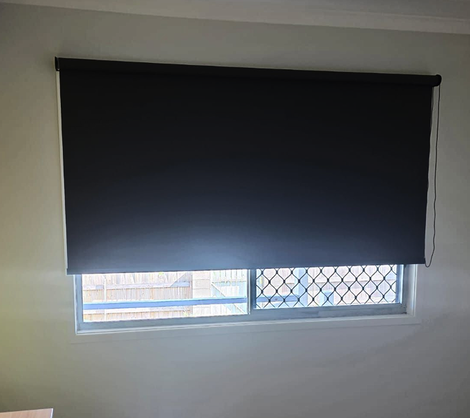A window partially covered by a black roller blind, revealing a security grille.