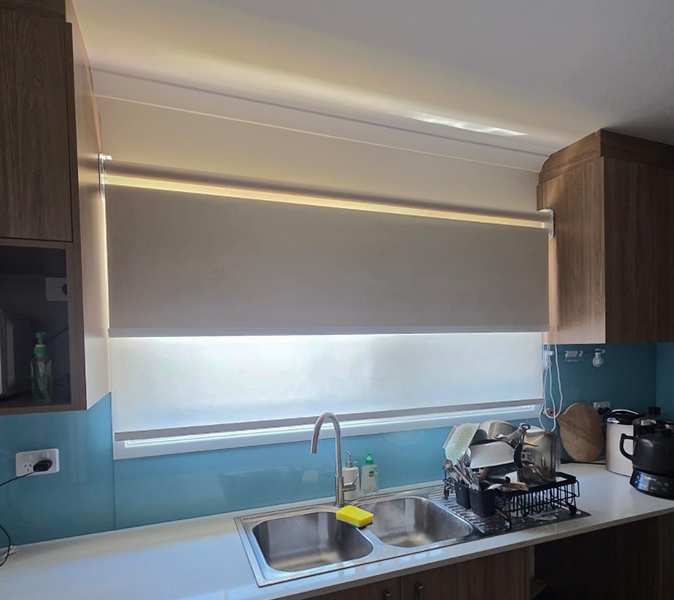 Kitchen sink under a window with a partially lowered roller blind.